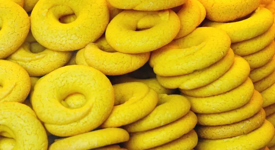 Una pila di dolcetti veneziani gialli, a forma di ciambella, con una texture leggermente ruvida.