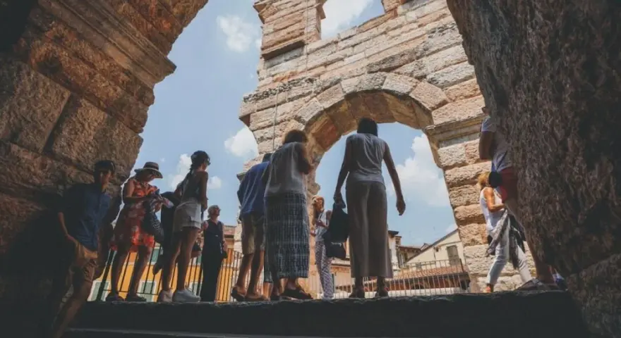 Turisti esplorano l'Arena di Verona, un'antica struttura che ricorda il Colosseo, sotto un cielo azzurro.