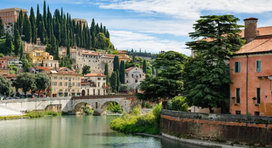 Un fiume attraversa Verona, con ponti storici e case colorate che salgono sulla collina. Un luogo incantevole da scoprire, tra le cose da vedere a Verona.