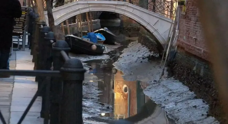 Canali di Venezia quasi asciutti, con barche arenate e riflessi di palazzi. Si vede quanto sono profondi i canali di Venezia in questa situazione insolita.