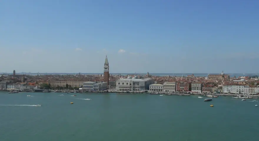 Venezia dall'alto, con il Campanile di San Marco che svetta tra i tetti rossi e il Canal Grande animato da vaporetti e barche.