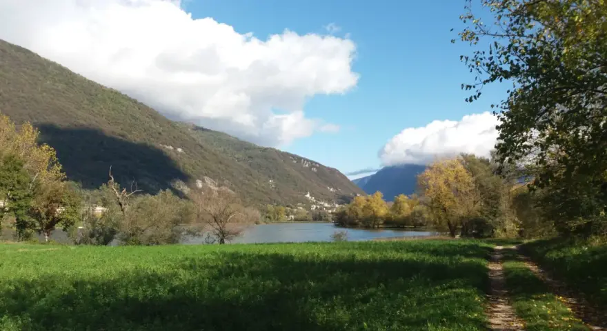 Sentiero per passeggiate in montagna Veneto, con lago, colline verdi e cielo azzurro con nuvole bianche.