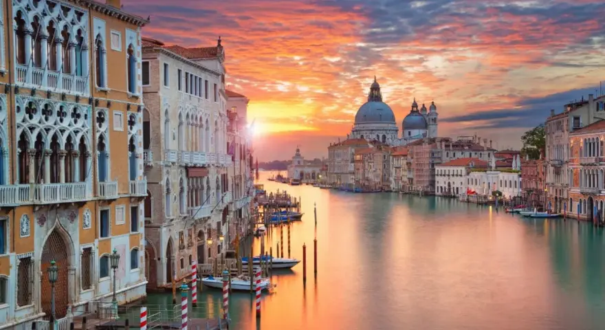 Tramonto sul Canal Grande, un quadro perfetto di posti romantici a Venezia. Palazzi storici e la Basilica di Santa Maria della Salute riflettono i colori del cielo.