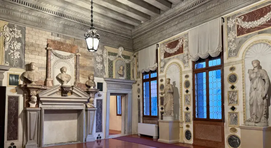 Interni del Palazzo Grimani: busti, statue, camino e finestre decorate in un salone sontuoso.
