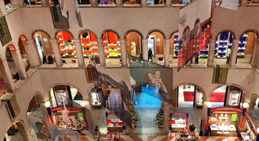 Interno del Fondaco dei Tedeschi, con archi, negozi e grandi stampe appese.