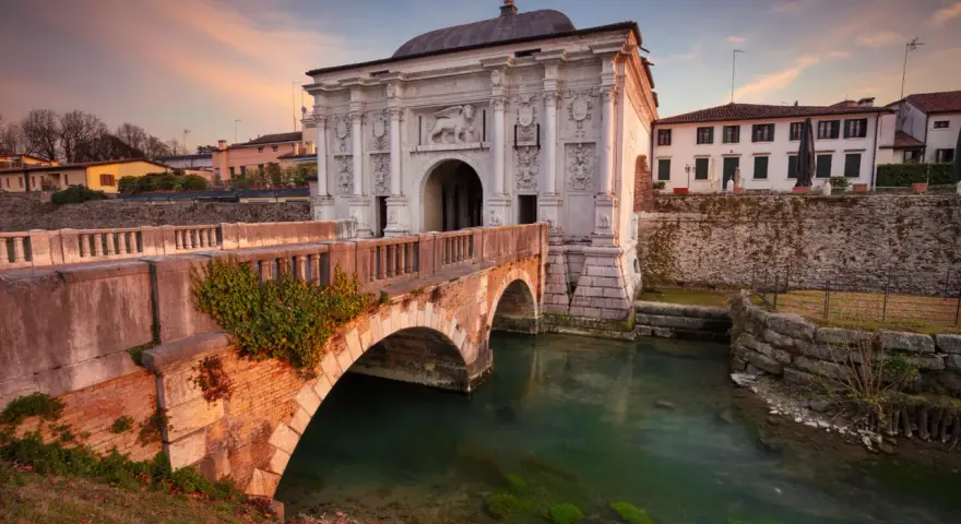 Porta San Tomaso a Treviso, un'idea per cosa fare a Treviso nel weekend. Un ponte in mattoni attraversa un canale con acqua verde.