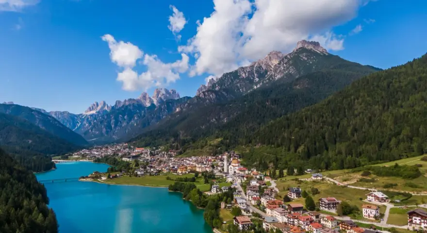 Vista aerea del **lago Auronzo di Cadore** con le montagne sullo sfondo e il paese che si affaccia sull'acqua turchese.