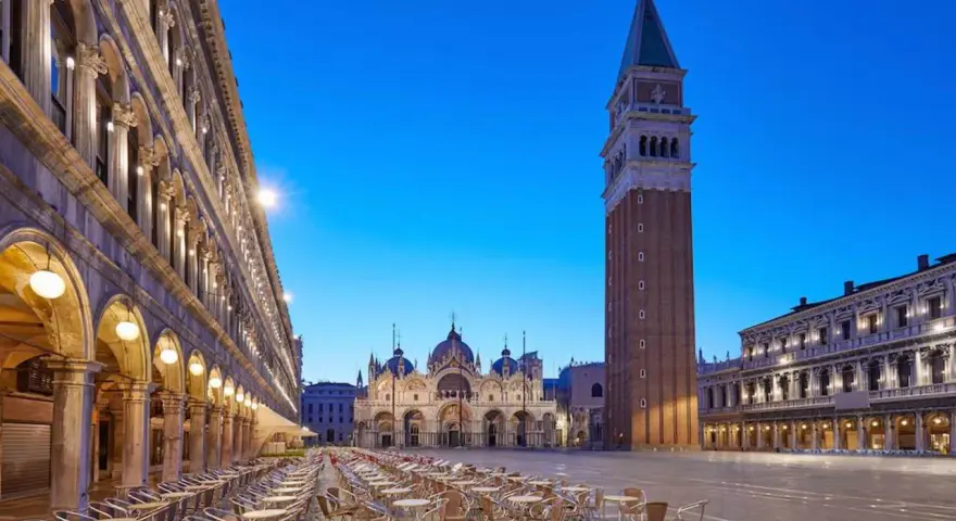 Piazza San Marco a Venezia, con la Basilica e il Campanile, testimoni della ricca storia della città. Tavolini all'aperto creano un'atmosfera serale.