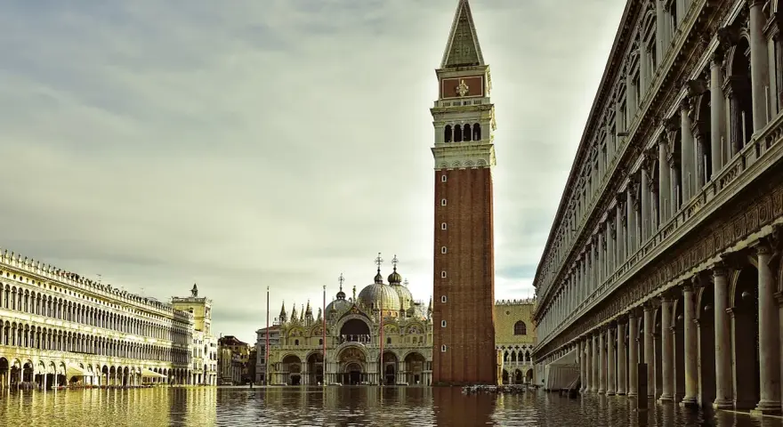 La maestosa torre di Piazza San Marco si erge sull'acqua alta, riflettendosi nel canale che lambisce i palazzi storici.