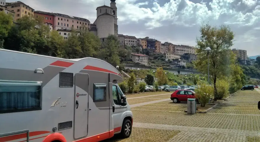 Camper in sosta a Belluno, con case colorate e un campanile sullo sfondo.