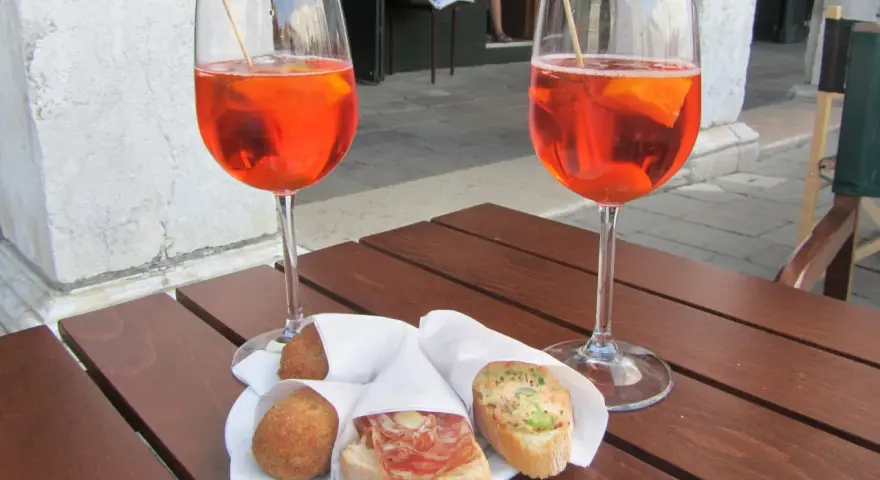 Due calici di Spritz e cicchetti, un classico per gli aperitivi a Venezia, su un tavolino di legno.