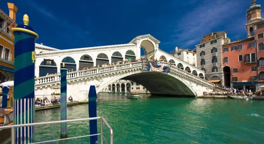 Ponte di Rialto, un'icona della storia veneziana, con le sue botteghe e la folla che lo attraversa, si specchia nelle acque verdi del Canal Grande.