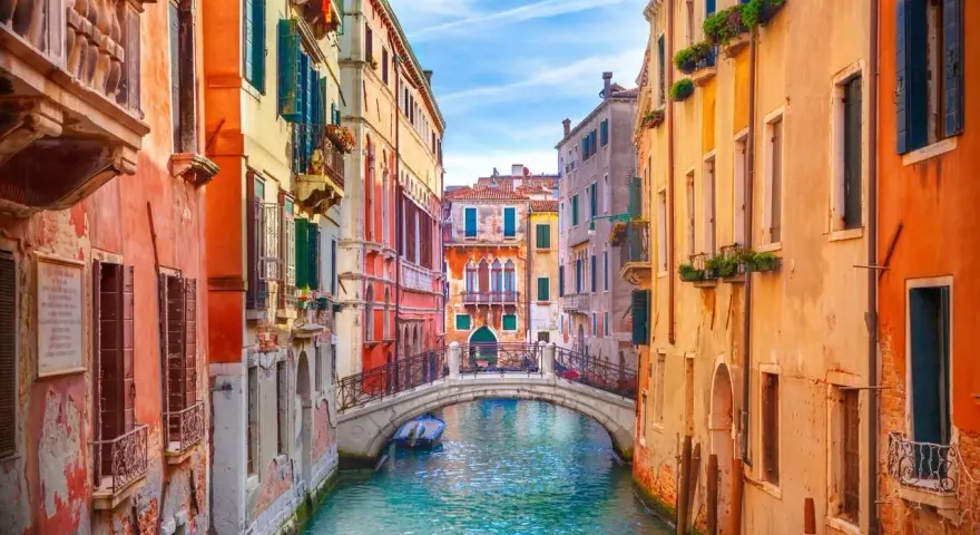 Canale veneziano con palazzi colorati e un ponte. Si immagina come fu costruita Venezia, su palafitte e ingegno.