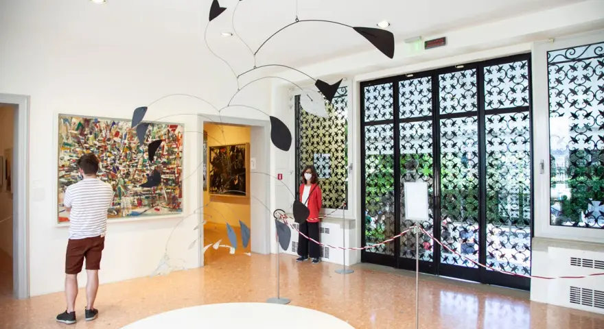 Un uomo ammira un quadro astratto, mentre una donna osserva una scultura mobile. Un'atmosfera d'arte al Peggy Guggenheim di Venezia.