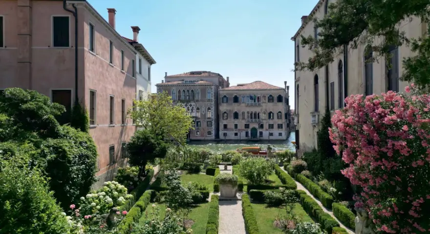 Giardini segreti a Venezia, con un canale e palazzi storici sullo sfondo. Un'oasi di pace tra il verde e i fiori.