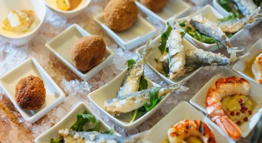 Assaggio di prodotti tipici veneziani: crocchette dorate, sarde fritte e gamberi grigliati, presentati su un letto di ghiaccio.