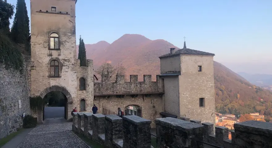 Antico borgo di Cison di Valmarino con torri e mura di pietra, sullo sfondo colline autunnali.