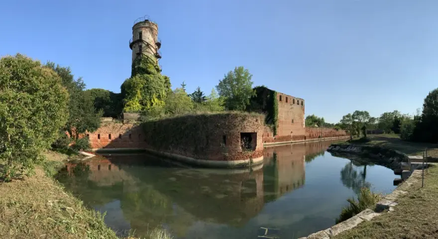 Antica torre e mura di mattoni circondate da un fossato, un angolo suggestivo di Venezia e dintorni, con vegetazione rigogliosa.