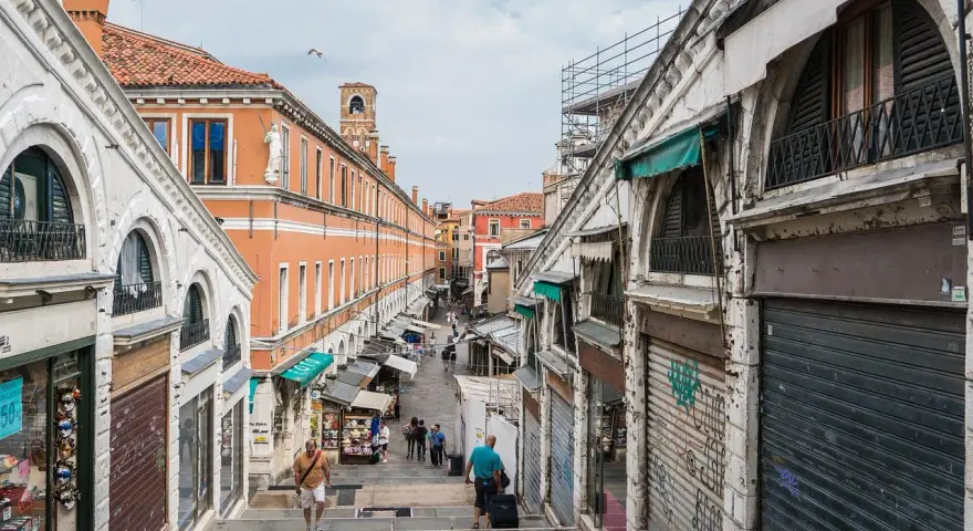Scendendo le scale del ponte di Rialto a Venezia, si intravede un mercato vivace con negozi e bancarelle.