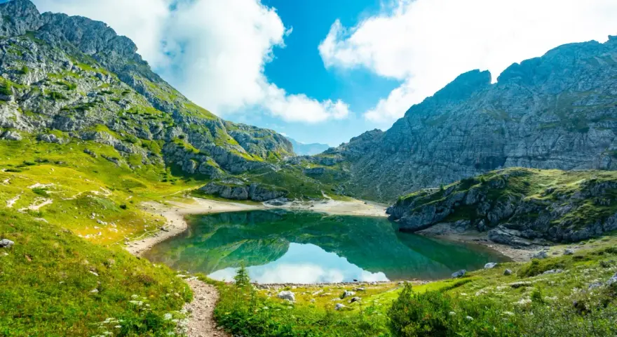 Sentiero panoramico verso un lago alpino turchese, incorniciato da montagne maestose. Un vero gioiello dell'alta via Dolomiti più bella.
