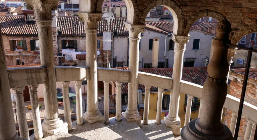 Dalla scala Contarini del Bovolo, vista sui tetti di Venezia. Colonne e archi in pietra creano un gioco d'ombre sulla gradinata.
