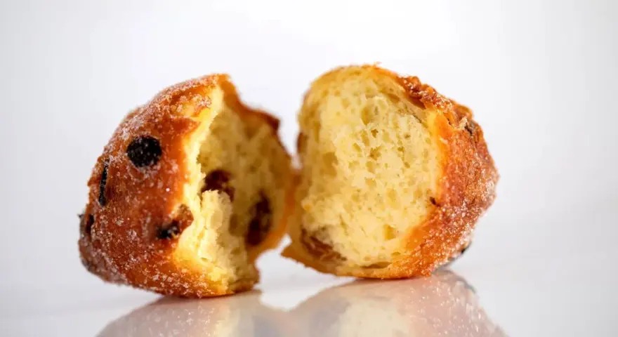 Frittelle veneziane, dolci e soffici, con uvetta e zucchero, spezzate a metà per mostrare l'interno invitante.