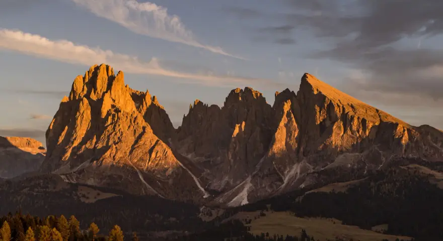 Le maestose **Dolomiti Rosse** illuminate dal sole al tramonto, con cime aguzze e pendii boscosi.