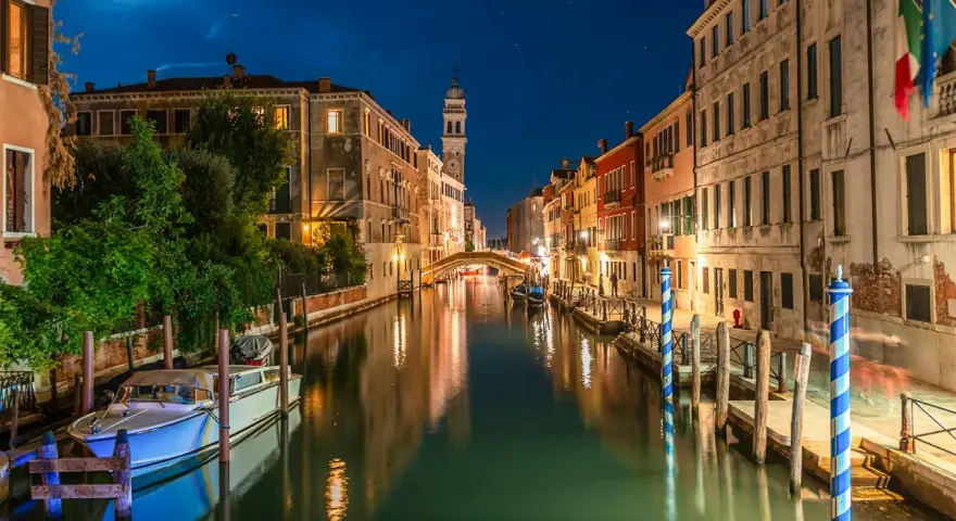 Una gondola venezia di notte, con luci soffuse che si riflettono sull'acqua e un cielo stellato.