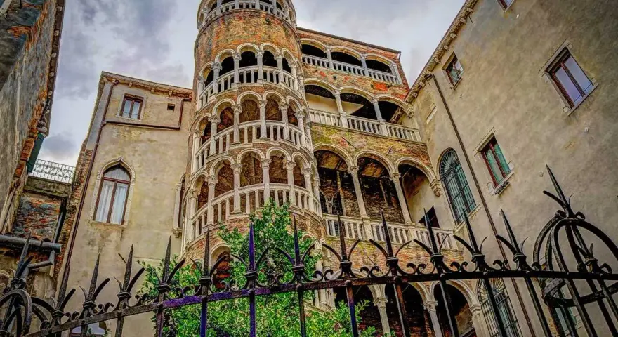 La scala chiocciola di Venezia, con i suoi archi e balconi, si erge maestosa tra antichi palazzi.