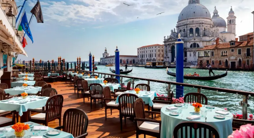 Tavoli apparecchiati con tovaglie azzurre e fiori arancioni, affacciati sul Canal Grande, con gondole e la Basilica di Santa Maria della Salute. Un'ambientazione da sogno per i migliori ristoranti di Venezia.