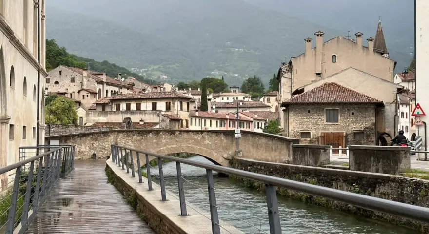 Passeggiata lungo il canale, tra antichi palazzi e ponti in pietra. Ecco cosa vedere a Vittorio Veneto, con le montagne sullo sfondo.