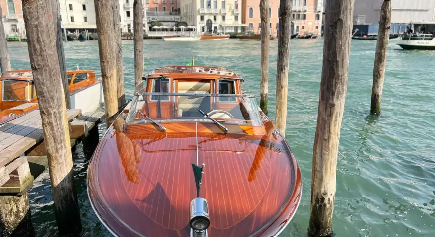 Un elegante taxi boat in legno lucido attende sul Canal Grande a Venezia, pronto a trasportare passeggeri tra i palazzi storici.