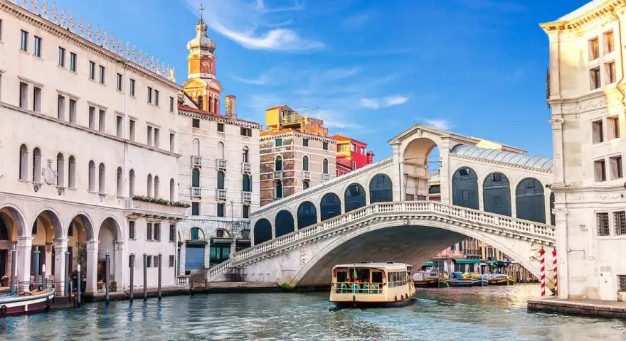 Venezia, il Canal Grande con il Ponte di Rialto e il Fondaco dei Tedeschi sullo sfondo. Una motonave naviga sull'acqua.