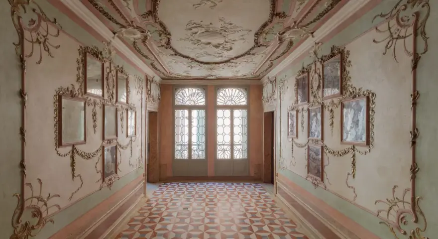 Corridoio decorato con stucchi dorati e specchi, soffitto affrescato e pavimento a rombi. Un assaggio dell'eleganza del Casino Venier.