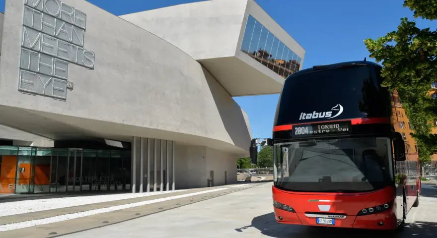 Autobus Itabus rosso e nero davanti a un edificio moderno con la scritta "More Than Meets The Eye". Un viaggio da Verona a Jesolo?