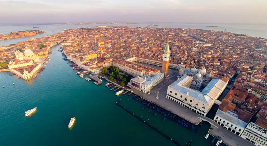 Vista aerea di Venezia al tramonto, con la Basilica di San Marco e il Palazzo Ducale che dominano la scena.