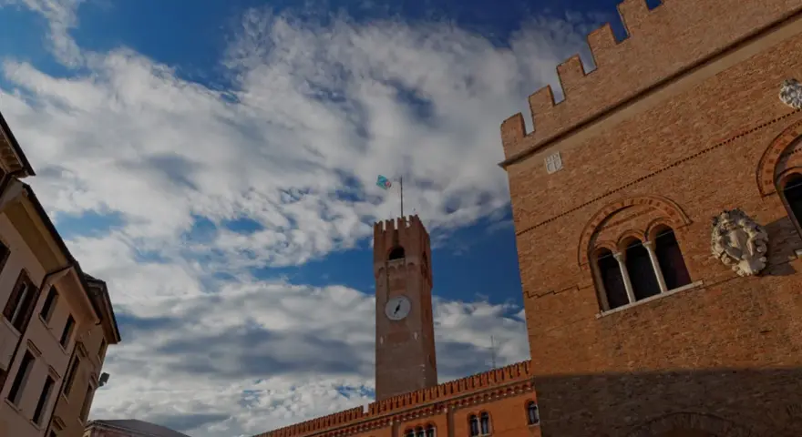 Torre dell'Orologio e palazzi storici a Treviso, un viaggio da Padova a Treviso sotto un cielo azzurro e nuvoloso.