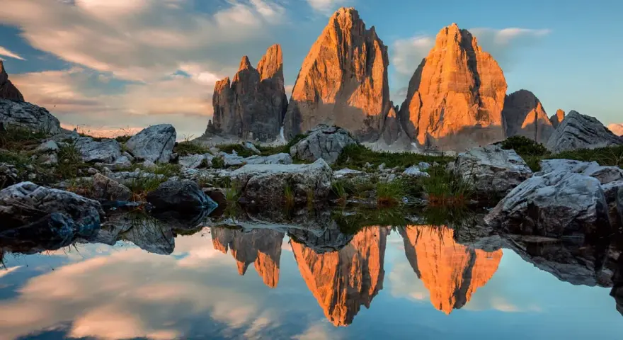 Le Tre Cime di Lavaredo illuminate dal tramonto, riflesse in uno specchio d'acqua. Un paesaggio che incarna la bellezza dei **Dolomiti paesi più belli**.