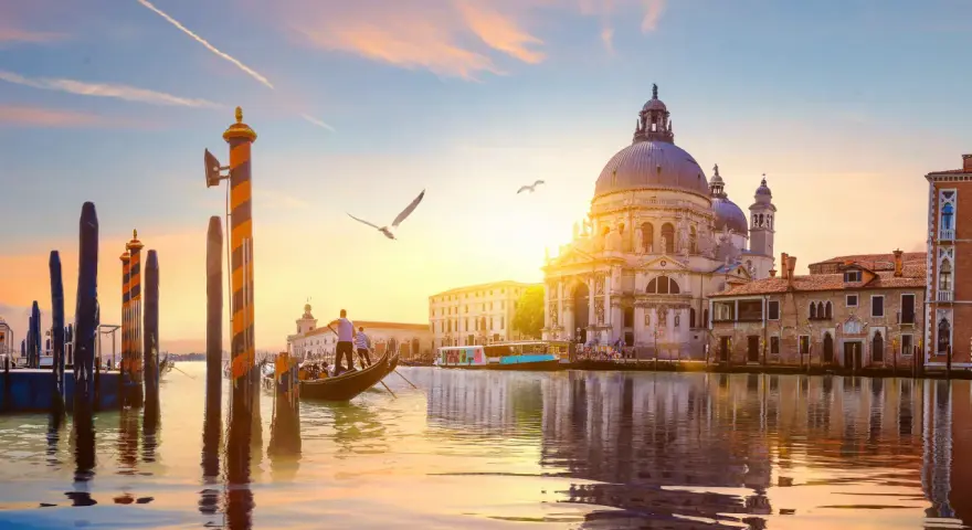 Gondola che scivola sull'acqua al tramonto, con la Basilica di Santa Maria della Salute sullo sfondo. Un'indimenticabile attività a Venezia.