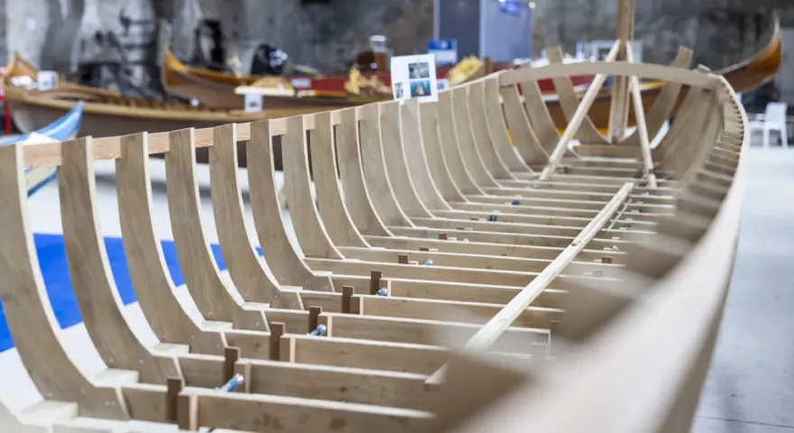 Struttura in legno di una barca veneziana in costruzione, con altre imbarcazioni sullo sfondo.