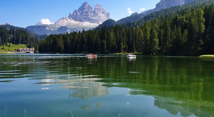 Il **lago di Misurina** incanta con le sue acque verdi e le montagne maestose. Barchette a remi solcano la superficie, riflettendo il cielo azzurro e la foresta di abeti.