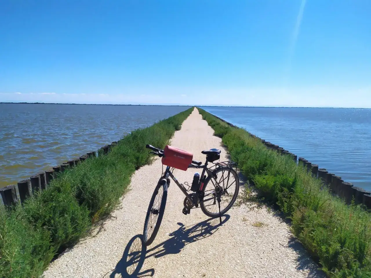Bicicletta su una strada sterrata che si estende all'infinito, fiancheggiata da acqua e vegetazione. Un percorso ideale per le ciclabili del Delta del Po.
