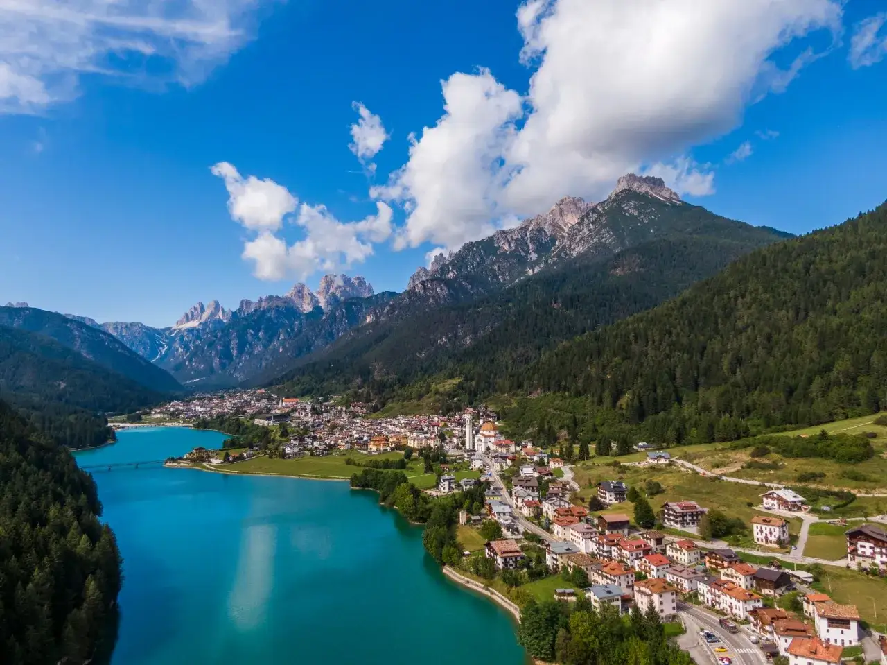 Vista aerea del lago Auronzo di Cadore con le montagne sullo sfondo e il paese che si affaccia sull'acqua turchese.