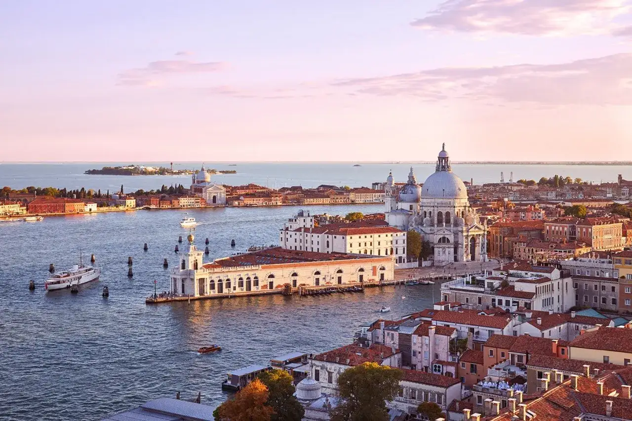 Vista aerea di Venezia al tramonto, con la Basilica di Santa Maria della Salute e la Punta della Dogana che si stagliano sull'acqua.