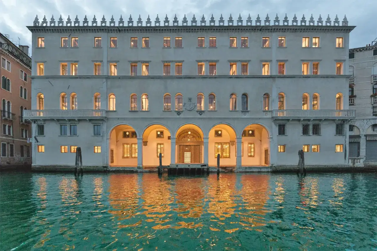 Il Fondaco dei Tedeschi a Venezia, con le sue finestre illuminate e il riflesso dorato sull'acqua, evoca un'atmosfera magica, quasi come una terrazza sul Canal Grande.