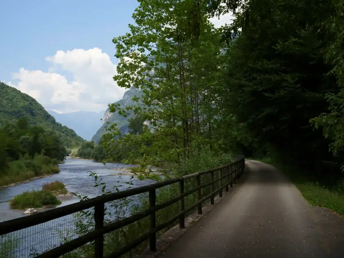 Sentiero panoramico lungo il fiume, ideale per una pedalata sulla ciclabile del Brenta. Montagne verdi e cielo azzurro.
