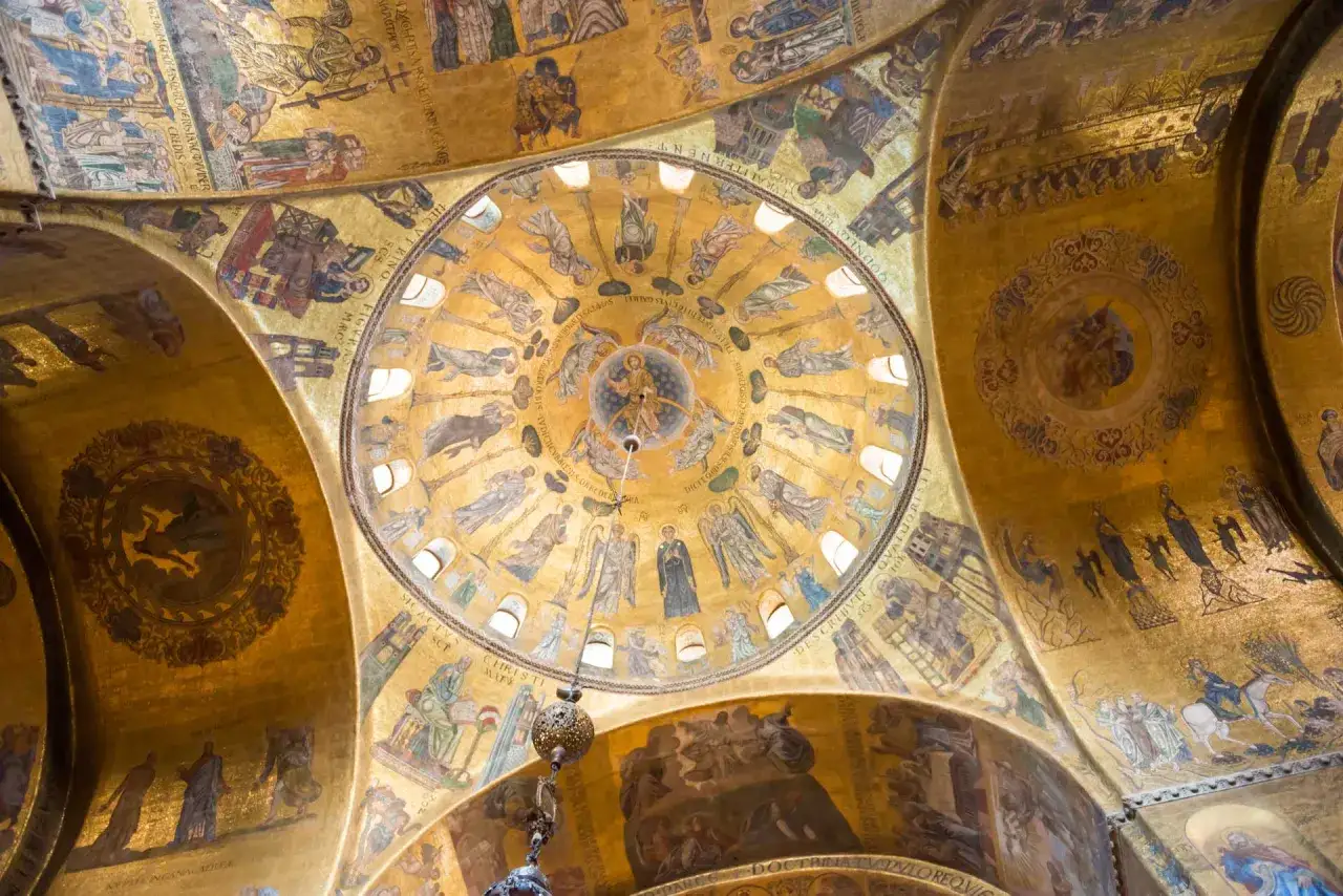 Mosaici dorati che ricoprono le volte di una chiesa, un esempio di famous art in Venice. Scene bibliche e figure sacre brillano sotto la luce.