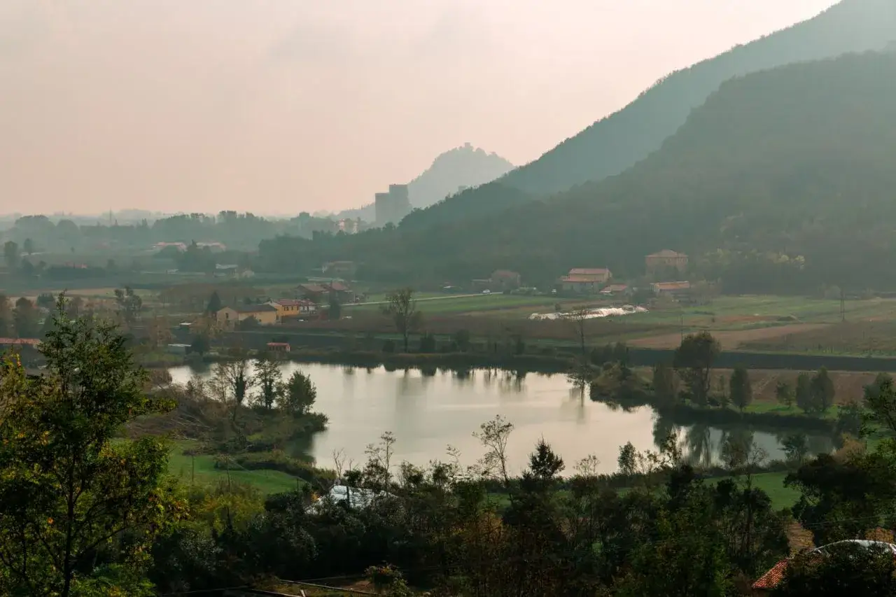 Paesaggio dei Colli Euganei cosa vedere: lago, colline boscose, campi coltivati e antichi borghi con torri in lontananza.