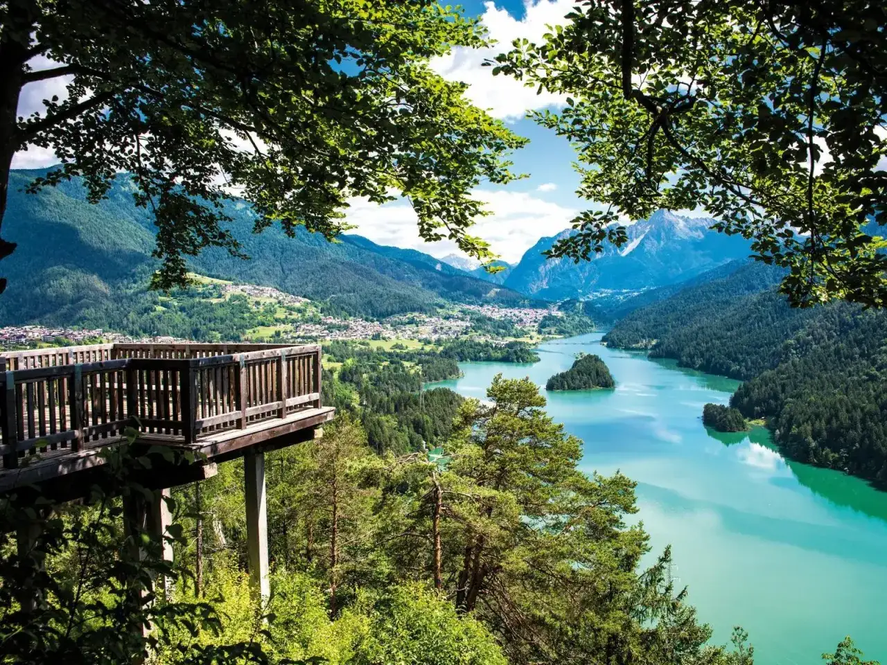 Balcone panoramico sui laghi del Cadore, con montagne sullo sfondo e un'isola verde nel lago turchese.