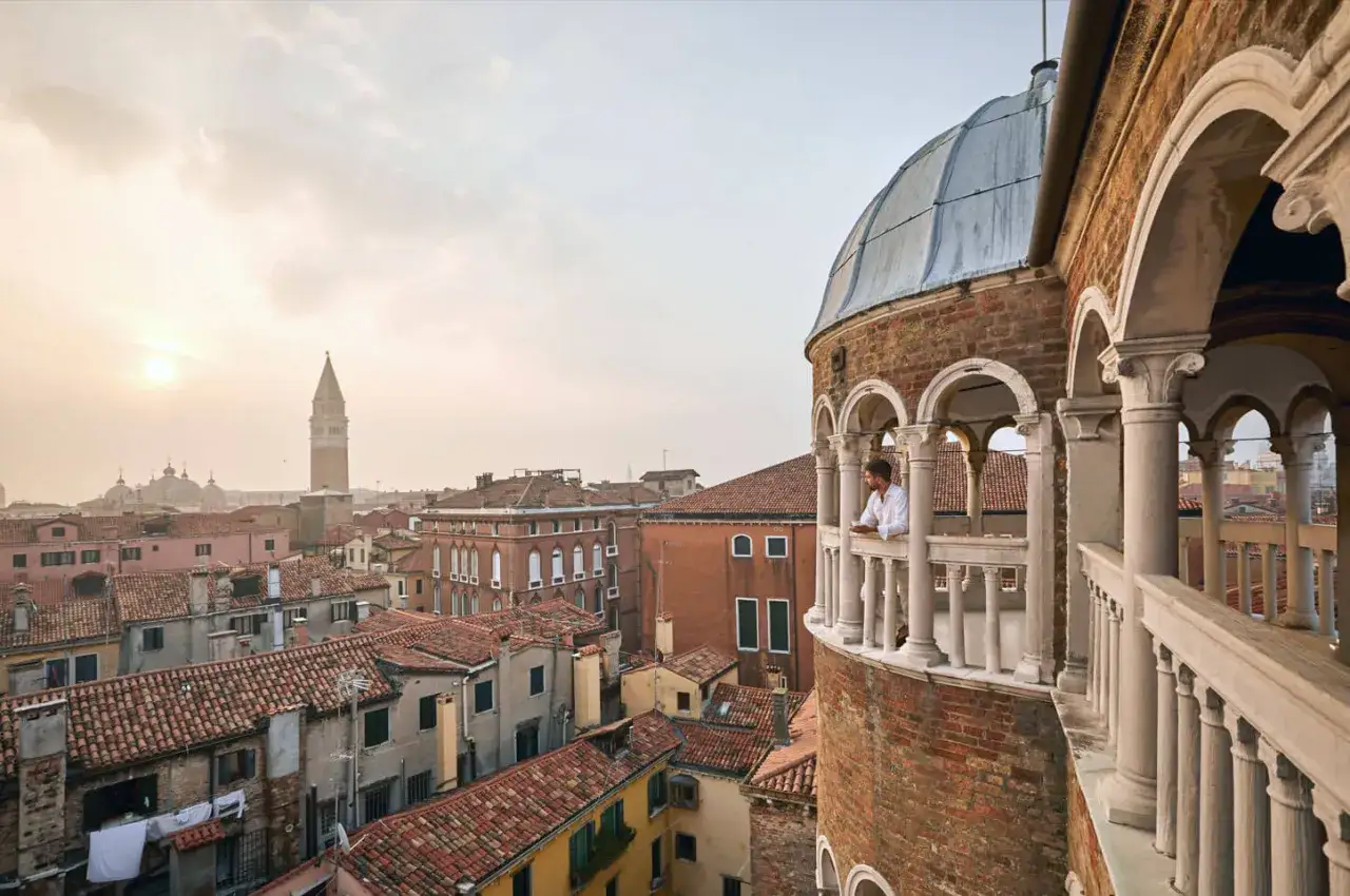 Uomo su balcone con vista sui tetti di Venezia. La scala chiocciola Venezia porta a questo panorama mozzafiato.